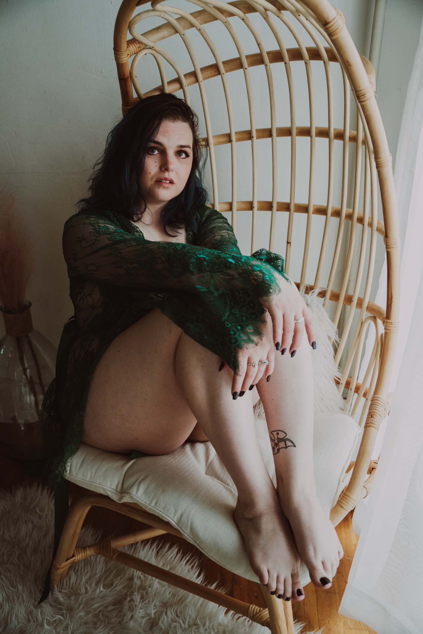 woman in green sits comfortably on a wicker chair while she is captured during an empowering boudoir session