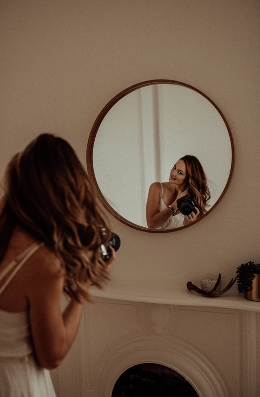 boudoir photographer flips her hair in the mirror to illustrating a pose for her client during a session