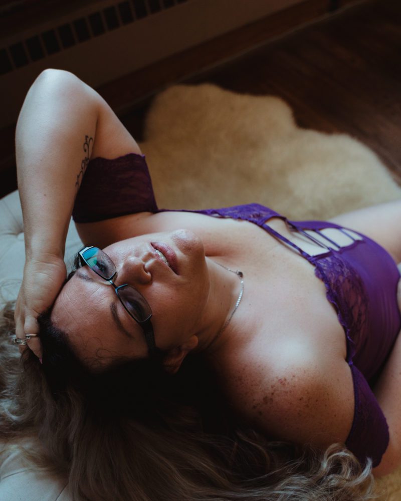 woman in purple lingerie relaxes against a couch while staring at the ceiling as documented by her boudoir photographer