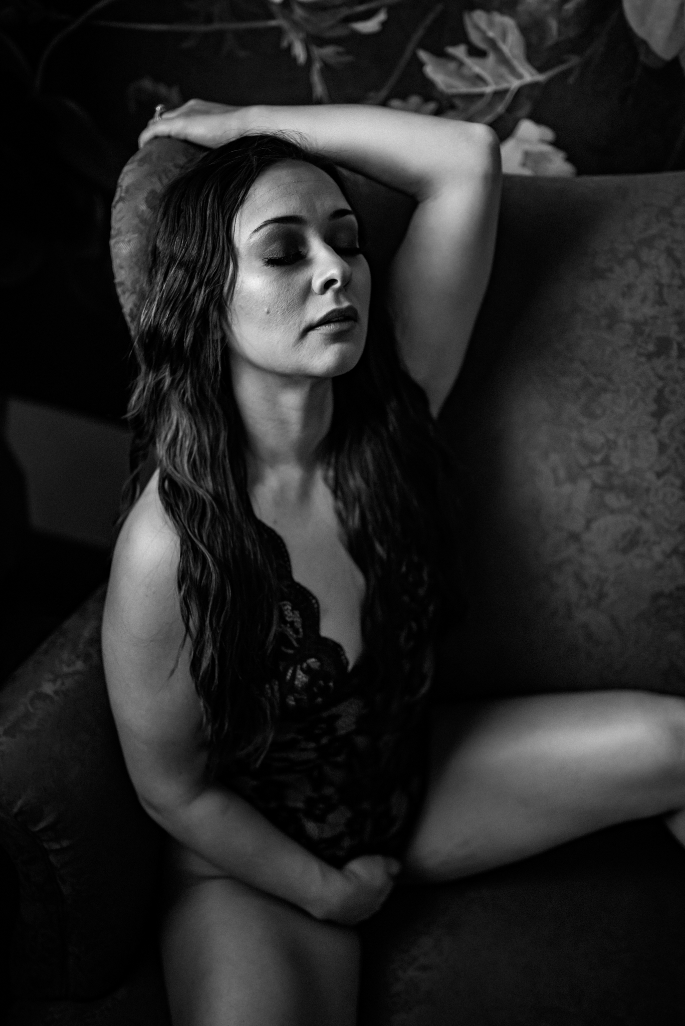 Black and white boudoir photo of a woman in a black lace bodysuit with her eyes closed during her kimberly ann boudoir experience session