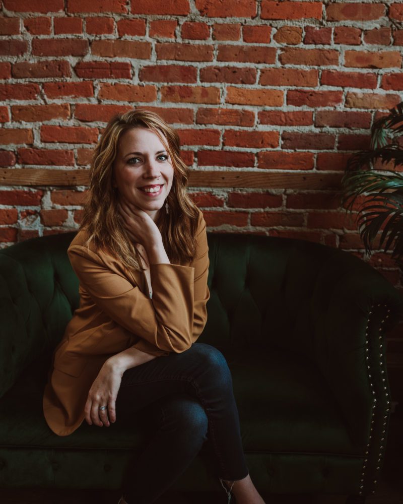 woman sits casually on a couch while she gets headshots taken to use in marketing her business