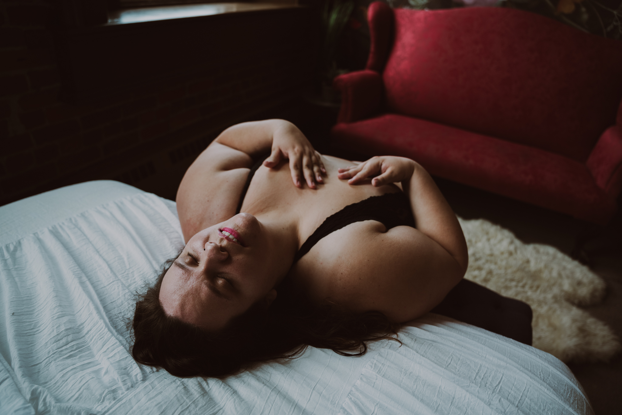 woman leans back onto the edge of a bed while being photographed during an intimate portrait session