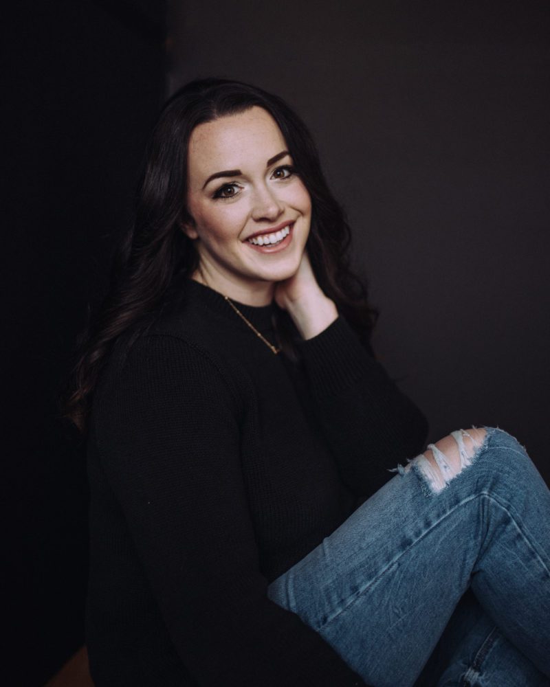 woman in a black sweater and jeans smiling at the camera while capturing luxe headshots for her business