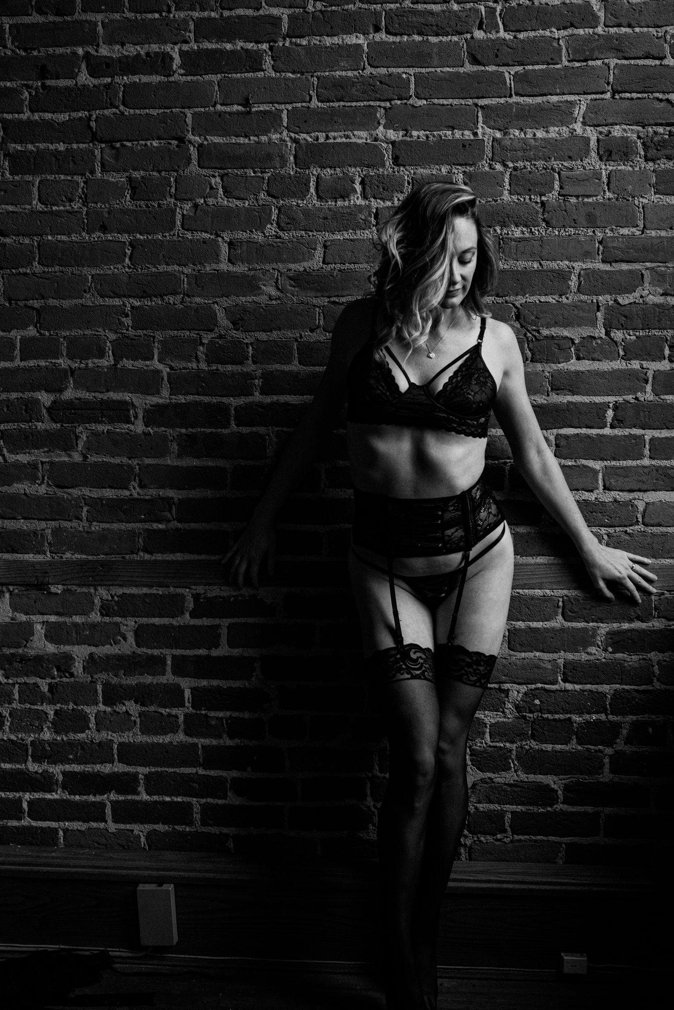 gorgeous black and white photo of a woman in a black lingerie set posing against a brick wall for a boudoir photo